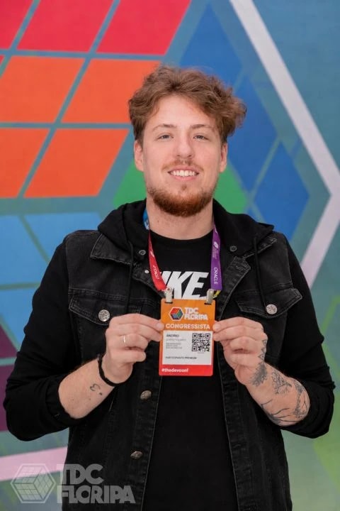 Andrio Siefert sorrindo, segurando o crachá de congressista do TDC Floripa